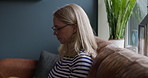 Laptop, relax and a woman reading on a sofa in the living room of her apartment on the weekend. Computer, face and glasses with a happy mature person chilling alone in her apartment in the morning