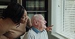 Window, caregiver and senior man with communication, pointing and view from retirement home. Nurse, support and healthcare with kindness and empathy of a woman nurse with conversation and talking