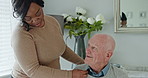 Caregiver helping senior man with jersey in the living room of modern nursing home for assistance. Bonding, smile and black woman nurse with elderly male person in wheelchair at retirement house.