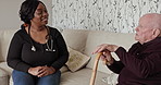 Woman, nurse and talking to senior patient on sofa with kane for healthcare, support or checkup at old age home. Happy female person, doctor or caregiver consulting elderly man on living room couch