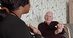Conversation, healthcare and nurse with elderly man with a walking stick in living room of house. Communication, medical and African caregiver talking to senior male patient in retirement home.