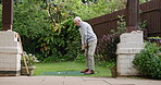 Golf, swing and senior man in backyard for sports, training and relax with hobby on artificial grass. Game, putting course challenge and club on green lawn with stroke, hit and ball in garden of home