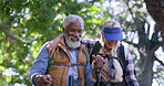 Senior, couple and walking with stick in nature for retirement wellness, hiking or hugging on trail. Interracial people, laughing and talking in woods for fitness, bonding or funny joke with backpack