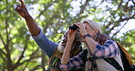 Senior couple, bird watching and hiking with adventure, pointing or forest with binoculars. Trekking, healthy old man or mature woman with fitness, interracial or woods with journey, nature or travel