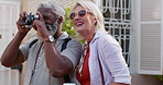 Mature couple, laughing and camera for photography with bonding or fun, break and summer holiday. People, multiracial relationship and outdoor as tourist on road for vacation, honeymoon and memories