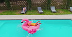 Holiday, jump and man in pool with flamingo, outdoor fun and playful summer in backyard from drone. Swimming, playing and people in water on vacation with inflatable toys, energy and poolside garden