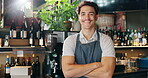 Barista, face and man with arms crossed in restaurant for customer service, laughing and career confidence. Waiter, person and happy entrepreneur in bistro for small business, hospitality and pride