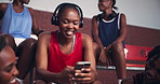 Sports girl, headphones and typing with phone on bench for music playlist, training break or laughing for chat. Basketball team, black person or smartphone subscription for streaming service or radio