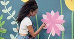 Mural, woman and painting art on wall for creative design, flower decor and volunteer. Artist, girl and painter outdoor with brush for community project, floral color and back for charity with wind