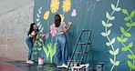 Happy, people and painting mural on wall for creative decoration, community project and artistic freedom. Women, artist and diy with public art, flower design and local culture for therapeutic hobby