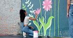 Art, woman and painting flower on wall for creative design, decoration and volunteer with friends. Artist, girl and painter outdoor with brush for community mural, floral color and back for charity