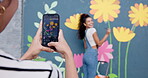 Painter, phone screen and photograph of woman with mural on wall for community art project. Artistic, creative and smile of happy person painting outdoor in city for decorating neighbourhood