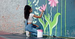 Artist, woman and painting flower on wall for creative design, decoration and volunteer in city. Art, girl and painter outdoor with brush for community mural, floral color or back for charity project
