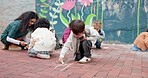 School, children and writing on playground with chalk for creative activity, fine motor skills or art lesson. Montessori, people and teacher with students for drawing patterns or learning development