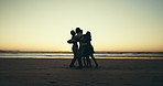 Hug, friends and people on beach at sunset for holiday, summer vacation and adventure together. Nature, travel and shadow of men and women by sea and ocean for freedom, happy and bonding on weekend