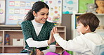 Education, high five or study with student and teacher in classroom together for development. Conversation, success or teaching with boy child and woman at desk in school for academic scholarship