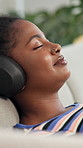Happy, black woman or relax with headphones for music, audio streaming or comfort on sofa at home. Female person, user or lying with sound, smile or app for playlist, album or entertainment at house