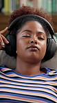 Black woman, relax and listening with headphones to music on sofa for audio streaming or comfort at home. Female person, user or lying with sound or app for playlist, album or entertainment at house