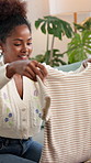 Happy, black woman and folding laundry with basket for housekeeping, washing or cleaning on sofa at home. Female person, housekeeper or cleaner with tshirt or clothing for hygiene or organizing