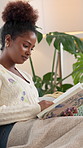 Happy, black woman and reading with book on sofa for story, fantasy or comfort in literature at home. Female person, reader or novel sitting with pages for new chapter or knowledge on couch at house
