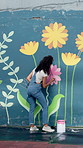Mural, woman and painting on wall for art, flower decoration or student with creative design outdoor. City, color or artist with brush for community project, diy or back for floral hobby with culture