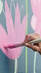 Person, hands and stroke with paintbrush with wall art for floral design, colorful creativity or community service. Closeup, volunteer or artist with paint for pink flower, mural activity or charity