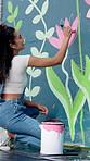City, woman and artist painting on wall for flower decoration, back and happy student with creative design outdoor. Art, color and painter with brush on mural for project, floral hobby and culture