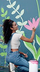 Outdoor, woman and artist painting on wall for flower decoration, back and happy student talking. Art, color and painter with brush on mural for project, floral hobby and creative culture in city