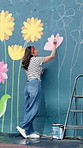 Outdoor, woman and artist painting on mural for flower decoration, back and volunteer with creative design. Art, color and painter with brush on wall for community project,  hobby and charity in city