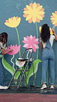 People, back and painting mural in city with helping hand for community project in town. Girl, together and friends with charity for social responsibility, design and volunteer by building by wall