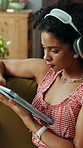 Headphones, tablet and woman on sofa in home on app for listening to music, podcast or radio. Digital technology, relaxing and female person streaming album, playlist or song in living room.