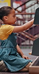 Girl, student and bookshelf with choice for story, novel or selection in school library. Child, kid or elementary learner with decision or books for knowledge, literature or childhood development 
