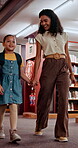 Smile, teacher and child talking in library for knowledge, studying and information for exam. Woman, girl and walking for education with books search, tutor helping and academic development at school