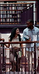 Happy, people and students walk in library with discussion, education and knowledge for team project. Man, woman and talking with books of college research, studying and learning assessment on stairs