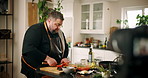 Man, chef or meal preparation with video camera for online tutorial, live recording or hospitality at home. Male person, influencer or streaming with ingredients in kitchen for recipe, tip or session