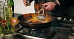 Hands, chef and flame with pan in kitchen for cooking with ingredients, spices and gourmet cuisine. Person, stove and fire with food, nutrition and seasoning for dish with vegetables at apartment