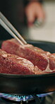 Recipe, hands and steak in frying pan in kitchen for meal preparation, enhance flavor or render beef moisture. Chef, person or meat protein with tweezer for healthy dinner, nutrition or food in home