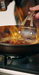 Hands, chef and flame with frying pan in kitchen for cooking with ingredients, meal prep and gourmet cuisine in home. Person, stove and fire with food, nutrition and seasoning for dish at apartment