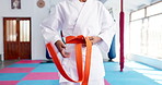 Person, hands and karate with orange belt for martial arts training, self defense or fighting skill level. Closeup, taekwondo or fighter getting ready with strap for promotion or experience in dojo