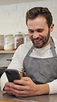Coffee shop, barista and man with phone for online sales, order update or check inventory. Mobile, cafe and happy waiter on internet for customer reviews, stock and typing message on social media