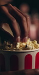 Person, hands and popcorn with movie in cinema at night for entertainment, show or film. Closeup, consumer or customer with food or snack in dark theater for suspense, eating or watching at center