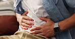 Hands, tummy ache and man on sofa in home for indigestion, diarrhea or food poisoning. Illness, sick and male person with stomach pain for constipation, IBS or abdominal muscle strain in house.