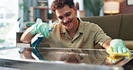 Happy man, detergent and cleaning table with spray for housekeeping, chores or disinfection at home. Male person, cleaner or maid with smile, gloves or cloth for bacteria or germ removal on surface