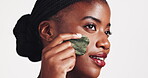Dermatology, black woman and gua sha on face for beauty, acne or blood circulation in studio on white background. Cosmetic, jade stone and product for lymphatic drainage, wellness and skincare