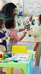 Hand painting, education and children in classroom at preschool for creativity, hobby or activity. Learning, students and group of kids with canvas for colorful art with high five for teacher.