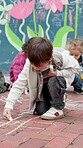 Child, student and chalk with writing at school, recess or break with art activity at Montessori kindergarten. Drawing, ground and boy with scribble, playground and fine motor skills development