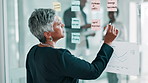 Business, glass wall and woman in office, writing and planning for profit growth, ideas and choice. Mature person, financial advisor and employee in workplace, sticky notes and calendar with decision