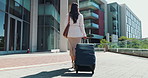 Business woman, walking and travel with suitcase for career journey or job opportunity in city. Back view, female person or employee with luggage for commute or immigration by corporate buildings