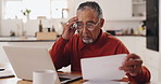 Senior man, laptop and documents in financial crisis for debt, mortgage or tax in kitchen at home. Elderly, male person or pensioner with computer or paperwork for finance, bills or expenses at house