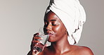 Beauty, towel and face of woman with drinking water for skin hydration, natural skincare and PH balance. Happy, black person and liquid on studio background for elasticity, anti aging and wellness
